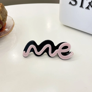 Minimalistische acetaat haarklem met roze me-letters op een gladde zwarte achtergrond