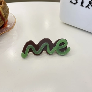 Detail van tweekleurige acetaat haarklem met groen golfpatroon en 'me' letter versiering
