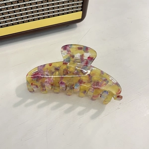 Detail view of large acetate claw clip with colorful floral pattern on white texture