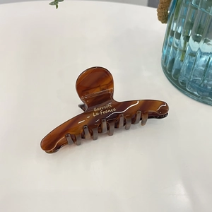 Elegante pinza per capelli in acetato tartarugato con scritte dorate su base bianca