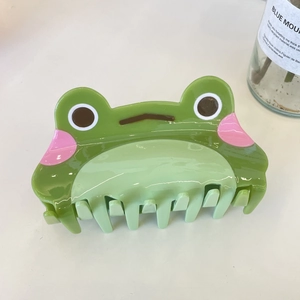 Cute green cartoon frog acetate hair claw clip with pink blush detail on a white surface