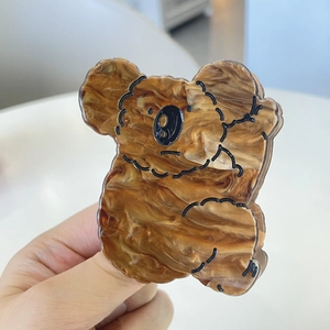 Détail d'une pince à cheveux koala en acrylique ambré marbré tenue à la main