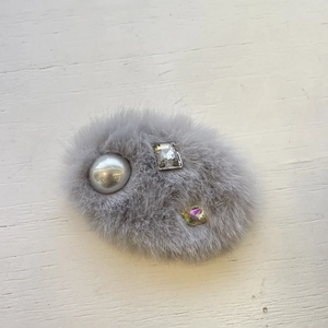 Barrette à cheveux grise en peluche avec perle et cristaux sur fond de bois blanc