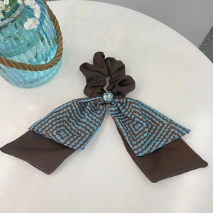 Brown bow scrunchie with blue wave pattern streamers and a square blue gemstone inlay
