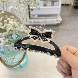 Detail of bow-shaped hair claw clip in black and white acrylic finish held by hand
