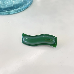 Macro detail of wave-shaped jelly hair clip in dark green with white cloud patterns