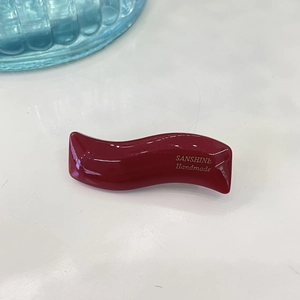 Detail of burgundy wavy hair clip with shiny finish and gold handmade lettering