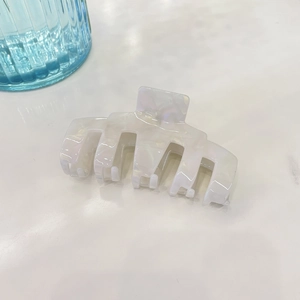 Detail of large acetate hair claw clip with white marble texture and iridescent finish