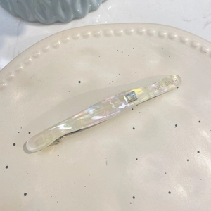 Détail d'une barrette en acétate crème perlé avec strass carré brillant et logo gravé