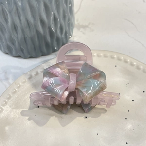 Macro detail of acetate bow hair claw with colorful marble texture and golden lettering