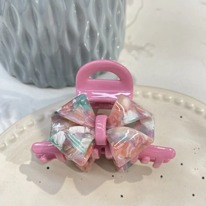 Detail of pink resin hair claw clip with marble texture acetate bow on beige plate