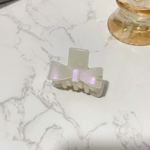 Close-up of elegant cream bow hair claw with pearlescent finish and gold lettering