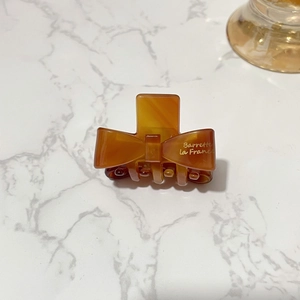 Elegant amber acetate bow hair claw clip with gold French lettering on marble surface