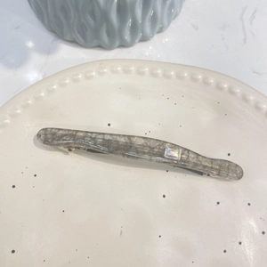 Détail de la barrette en acétate marbré gris avec strass et lettrage doré élégant