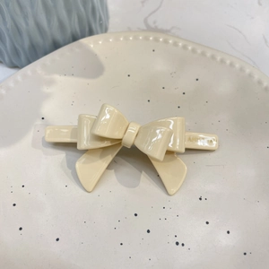 Close-up of a creamy white acetate bow hair clip on a minimalist ceramic jewelry tray