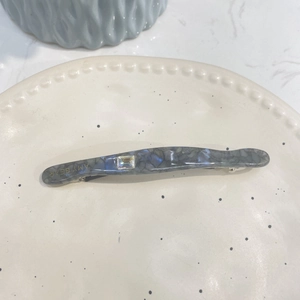Détail de la barrette en acétate marbré bleu avec cristal carré et lettrage doré