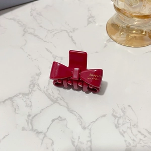 Elegant burgundy acetate bow hair claw clip with golden lettering on marble surface