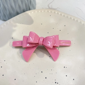 Pink acetate bow hair clip with Amy Bear gold lettering on a decorative cream plate