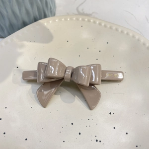 Close-up of mocha acetate bow hair clip with gold lettering on a ceramic tray