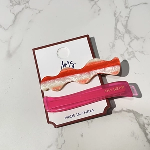 Detail view of wavy acetate hair clip and pink clip with gold lettering on marble
