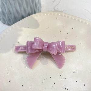 Detailed macro shot of a purple acetate bow hair clip with gold logo on a ceramic plate