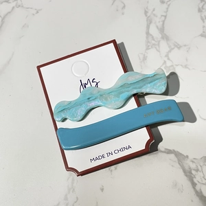 Detail of candy color wavy acetate hair clip set with gold logo on marble background