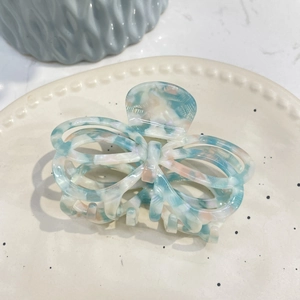 Elegant hollow butterfly hair claw in blue acetate marble finish on a ceramic plate