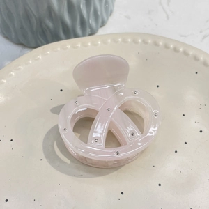 Pink acetate hair claw clip with bow shape and silver studs in a ceramic dish