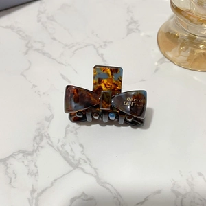 Detailed close-up of a tortoiseshell bow hair clip on a white marble background