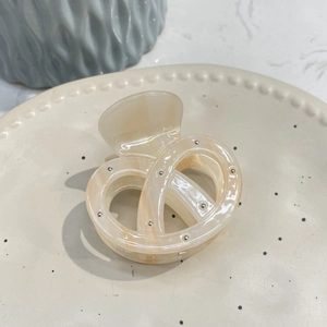 Detail view of a cream-colored acetate hair claw clip with silver bead accents on ceramic plate
