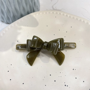 Detailed view of dark green acetate bow hair clip with gold logo on a ceramic tray
