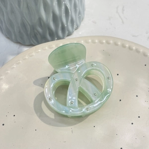 Detail view of a mint green pretzel-shaped acetate hair claw with silver metal studs