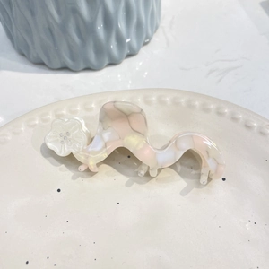 Pink marble acetate hair claw with white flower pattern on a wavy ceramic tray