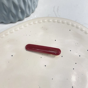 Elegant deep red acetate rectangular hair clip with gold label on a minimalist ceramic plate