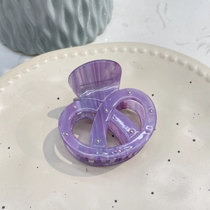Detail of purple marble acetate pretzel hair claw with silver studs on ceramic plate