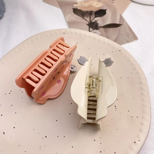 Gros plan de pinces à cheveux en acétate rose pastel et beige sur un plateau en céramique