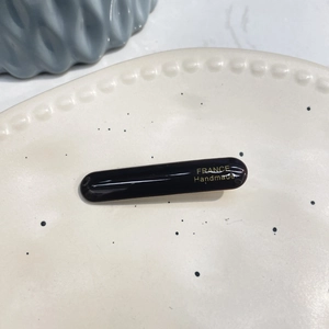 Detail of glossy black acetate hair clip with golden France Handmade lettering on ceramic