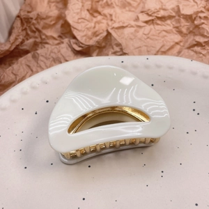 Detail view of cream white acetate hair claw with gold metal hinge on ceramic plate