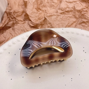 Elegant semi-circle acetate hair claw with amber pattern and golden metal teeth on paper