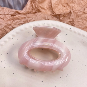 Pink marble acetate hair claw clip in oval donut shape on a ceramic tray display
