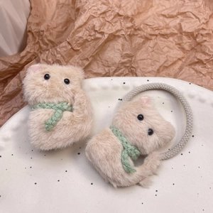Detalle del coletero y pinza de oso de peluche con bufanda verde en un plato de cerámica