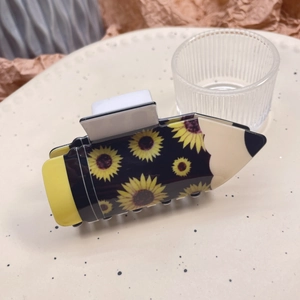 Close-up of pencil-shaped hair claw clip with sunflower pattern on acrylic surface