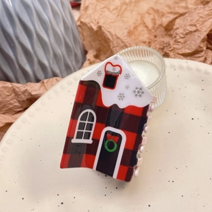 Close-up of a red plaid house hair claw clip with snow roof on a cozy ceramic plate