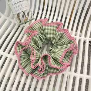 Close-up of green checkered scrunchie with pink lace trim and pleated fabric texture