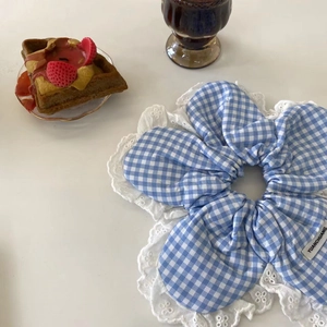 Detailed shot of blue plaid scrunchie with lace trim and woven label on a white background