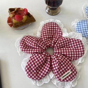 Detail of flower-shaped red gingham scrunchie with white lace edges on a styled table