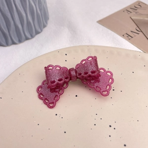 Detail view of a sparkling pink lace bow hair clip on a vintage beige ceramic plate