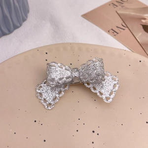 Close-up of silver glitter bow hair clip with lace edges on a ceramic display plate