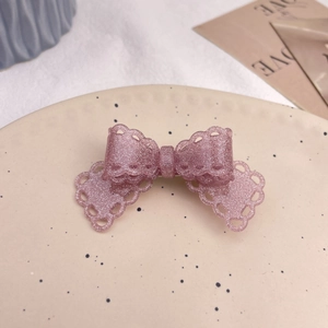 Detail of pink glitter bow hair clip with lace edges on a decorative ceramic plate