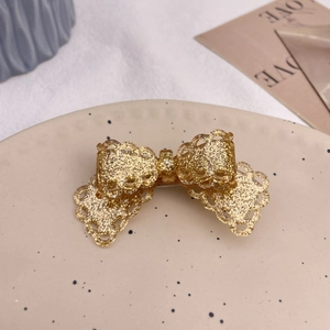 Detail of a lace-edged bow hair clip with gold glitter fill on a ceramic plate